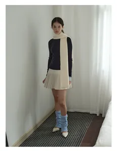 Full body shot of a model wearing a thick wool knit scarf with a white pleated mini skirt