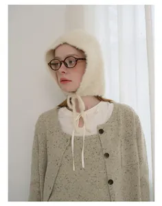 Detail of soft cream wool boucle hat with ties and textured knit cardigan for winter