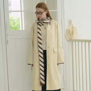 Morbida sciarpa in maglia a righe beige e marrone abbinata a un classico trench coat