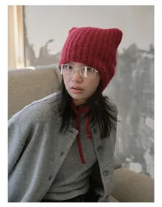 Detailed knit texture of red cat-ear beanie with soft chin straps in cozy indoor setting