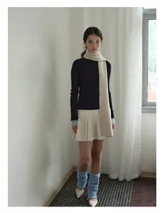 Close-up of soft beige wool scarf styled with dark blue knitwear and pleated skirt