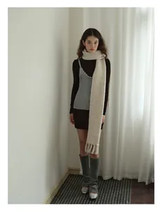 Full view of long beige wool blend scarf with fringe tassels on model in minimalist room