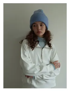 Detalle del gorro de lana azul claro de punto grueso con sudadera blanca de media cremallera