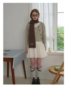 Detailopname van een bruine wollen sjaal gecombineerd met een beige vest en een rok