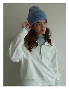 Detalle de gorro de punto azul cielo combinado con sudadera blanca en modelo