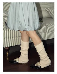 Detail of cream cable knit wool blend leg warmers styled with black glossy pointed shoes