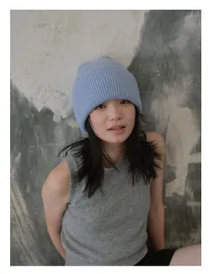 Detalle del gorro de punto azul claro y chaleco gris en una modelo ante una pared rugosa