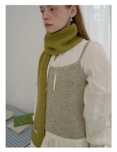 Detail van groene gebreide sjaal van 80% wol met zachte textuur en wit merklabel
