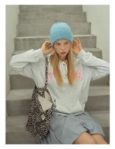 Detail of light blue wool knitted beanie paired with a pink bow hoodie and leopard bag