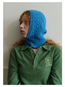 Detail of sky blue cable knit wool balaclava paired with green embroidered polo shirt