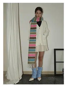 Détail d'une longue écharpe à rayures colorées et pompons portée par un mannequin en hiver