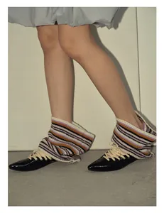 Close-up of black patent leather pointed shoes with colorful striped knit leg warmers