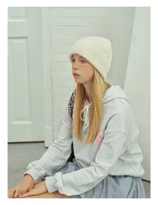 Close-up of a white chunky knit wool beanie paired with a casual grey hoodie outfit