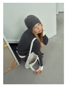 Dettaglio della trama del cappello in lana grigio scuro e cardigan con borsa di tela bianca