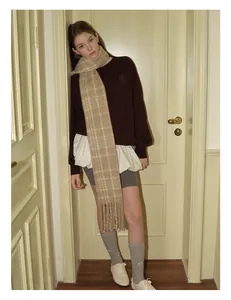 Detail shot of a beige plaid wool scarf with long fringes styled for a winter outfit
