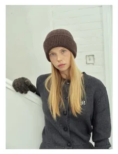 Detail showing deep brown thick knit wool beanie and grey cardigan with metallic logo