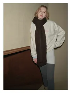 Dettaglio di sciarpa con frange in lana marrone scuro con felpa beige minimalista