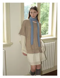 Detail eines blauen Strickschals aus Wolle über einem Vintage-Spitzenkleid und braunem Strick