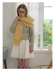 Close-up of bright yellow wool scarf with long tassels paired with knit cardigan