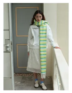 Détail d'une écharpe en laine à rayures jaune et vert avec franges sur tenue blanche