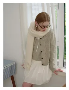 Detail of soft cream wool scarf with tassels and textured knit cardigan in a cozy winter style