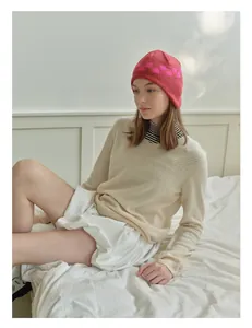 Detailed close-up of a pink checkerboard knit earflap hat worn in a cozy bedroom setting