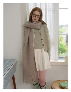 Brown fringe wool scarf paired with green cardigan and white skirt in cozy indoor setting