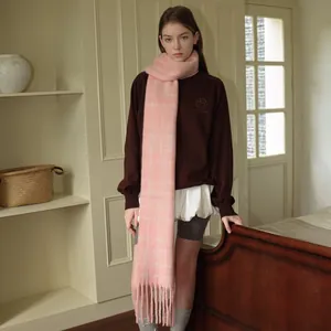 Pink checkered wool blend scarf with fringe tassels shown on a model in a cozy indoor setting