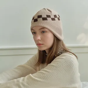 Beige checkered knit beanie with ear protection for women shown in soft indoor lighting