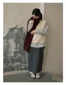Detail view of a burgundy red wool fringe scarf styled with a beige knit vest and grey skirt