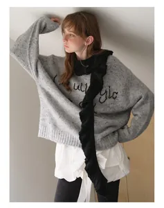 Detailed texture of light grey knit sweater with black embroidered script and ruffle scarf