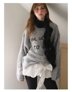 Detail of grey knitted sweater featuring black embroidery and a ruffled wool scarf