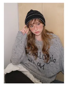 Detail of a soft striped knit beanie paired with a grey embroidered letter sweater