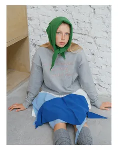 Detail of pink embroidered text on a grey long-sleeve sweatshirt paired with green knit scarf