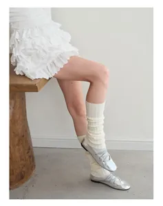 Detailed knit texture of cream wool leg warmers with silver metallic ballet flats
