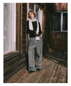 Detail shot of a cream cable-knit wool scarf paired with a black sweater and grey trousers