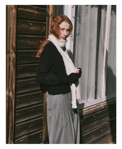 Detail of white wool blend cable knit scarf styled with grey trousers and black sweater