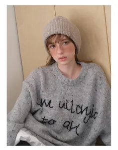 Detail of beige knitted beanie hat paired with grey embroidered alpaca blend sweater