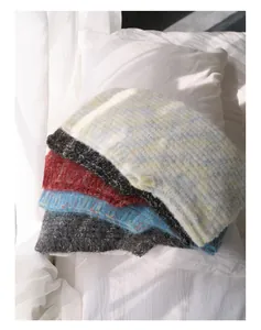 Dettaglio di passamontagna in misto lana colorati impilati su un letto bianco al sole