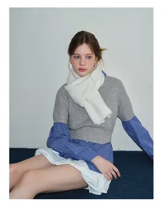 Close-up of white chunky knit wool scarf paired with a grey knit top and plaid shirt