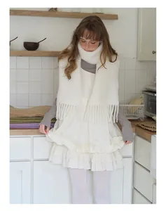 Detail of white ruffled layered dress with white tasseled fringe alpaca wool blend scarf