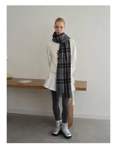 Full body view of a grey plaid wool scarf with tassels in a minimalist winter outfit