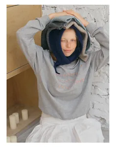 Detailed view of pink embroidery on grey sweatshirt with layered knitted scarves