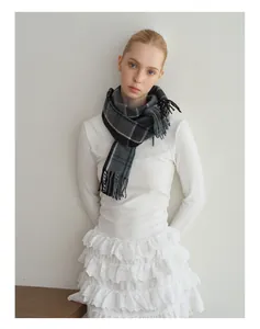 Detailed view of the soft grey plaid wool scarf featuring fringe tassels on the hemline