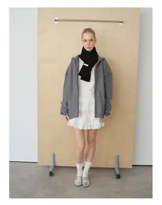 Detailansicht eines schwarzen Strickschals aus Wolle mit weißem Label und grauem Hoodie