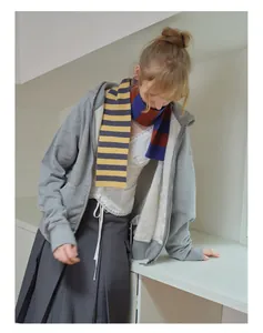 Detail of a thin merino wool striped scarf paired with a grey hoodie in a preppy style