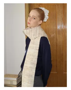 Close-up of a gradient wool blend scarf with fringe and a large white floral hair tie accessory
