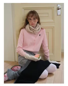 Détail d'un cardigan en laine tricotée rose avec logo noir et accessoire écharpe beige