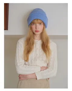 Detail of blue rib-knit beanie paired with a cream wool-blend cable knit cardigan