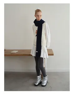 Detail eines langen dicken Strickschals mit weißem Etikett und bestickter Weste